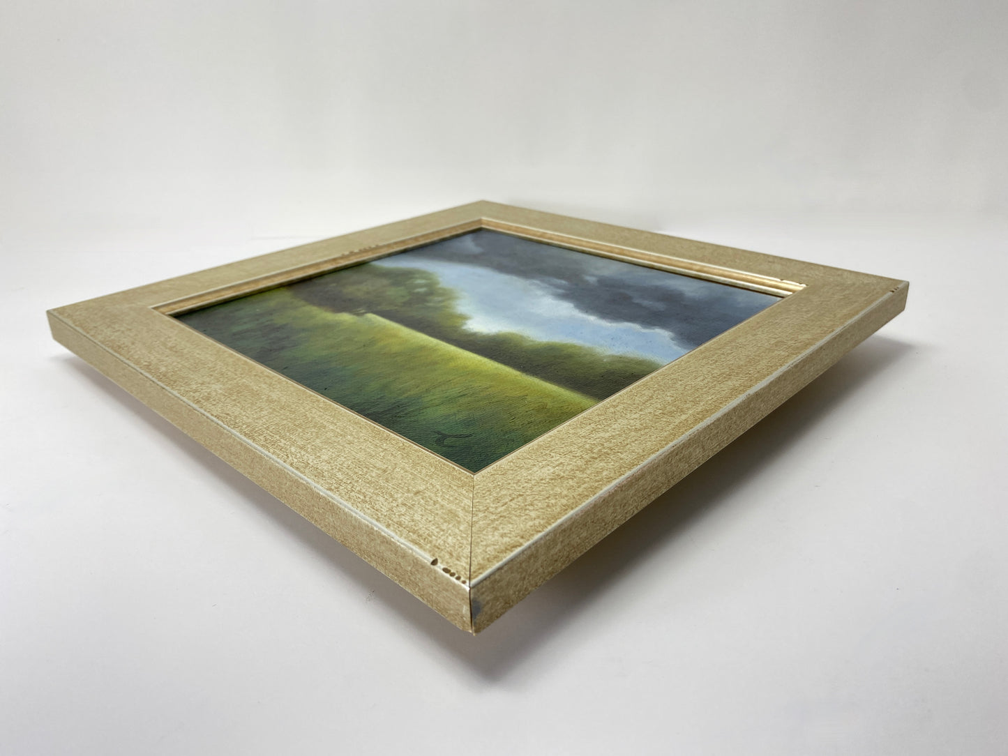 Framed original oil artwork of a landscape with green fields and blue sky on a white background