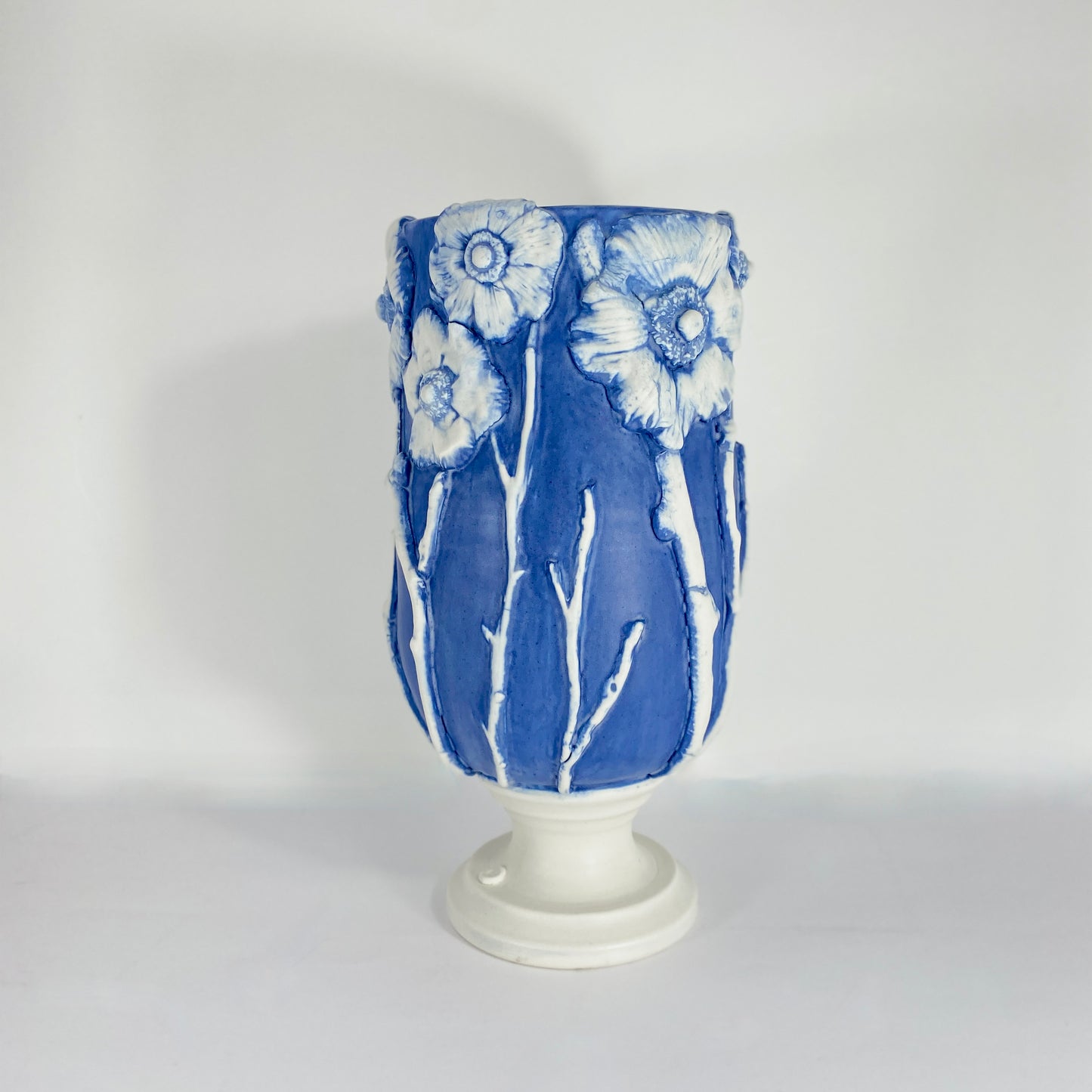 Product image shot of hand-thrown porcelain vessel in deep cobalt blue, with white anemone flowers in relief around the rim
