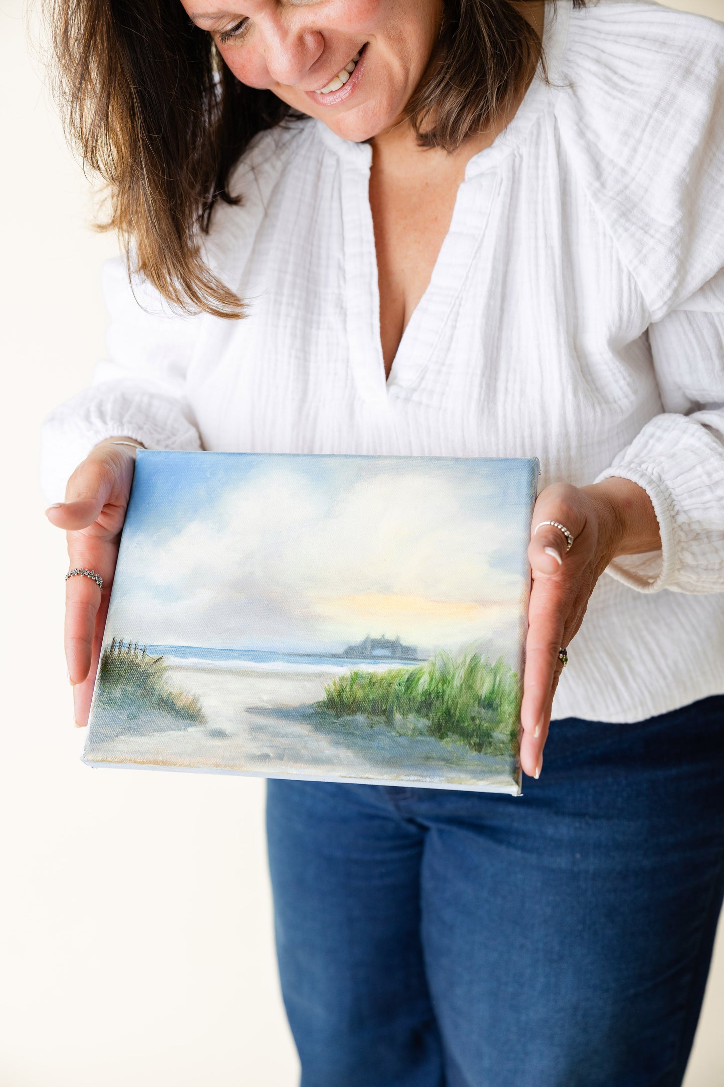 Artist Carla Thomson holding a small painting of a Narragansett beach scene