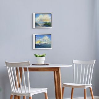 Dining room with a wooden table and white chairs, featuring two framed artworks of RI coast - Narragansett Towers and Goat Island Lighthouse Newport, on the wall.