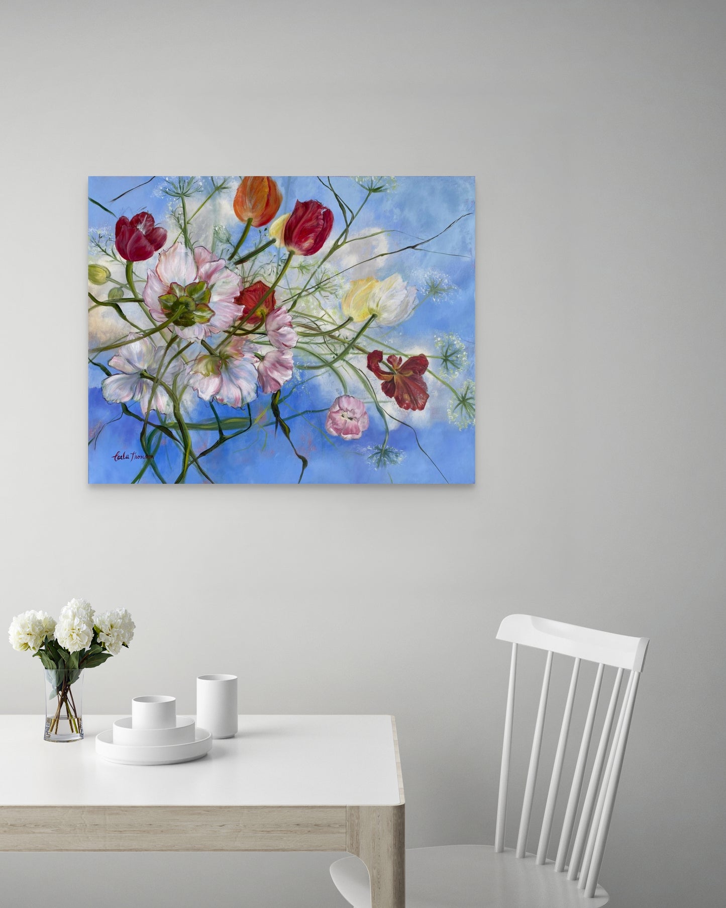 Floral painting on a wall above a table with a vase of flowers.