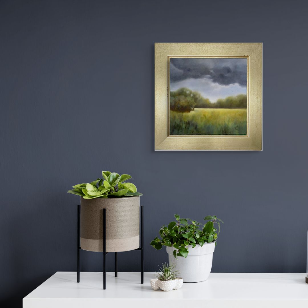 Framed original oil landscape painting on a dark blue wall with potted plants below.