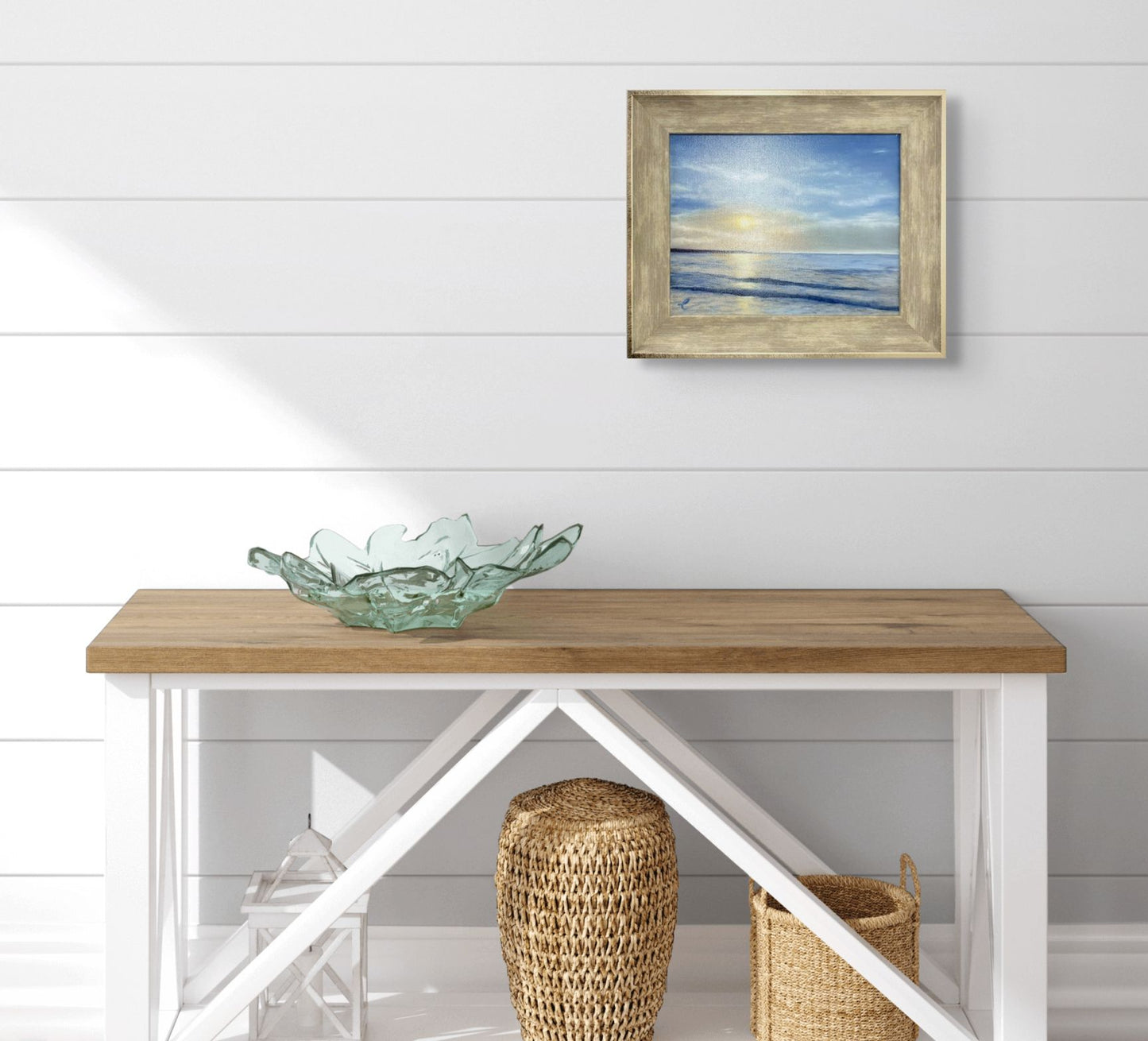 Wooden console table with a glass bowl and woven stools against a white wall with an original oil painting of Narragansett Beach, RI.
