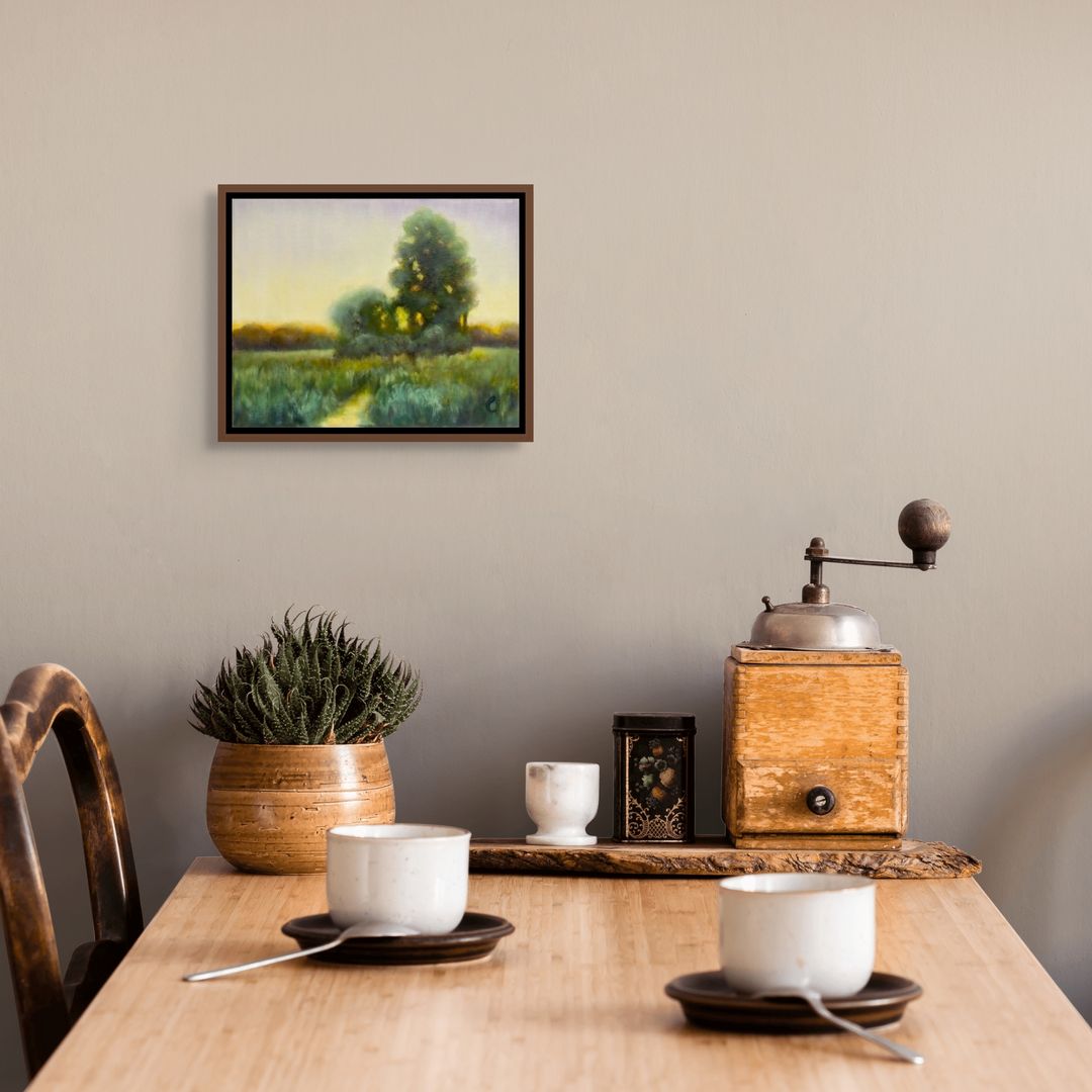 Wooden table with coffee cups, a coffee grinder, and a potted plant against a beige wall with a framed original oil landscape painting.
