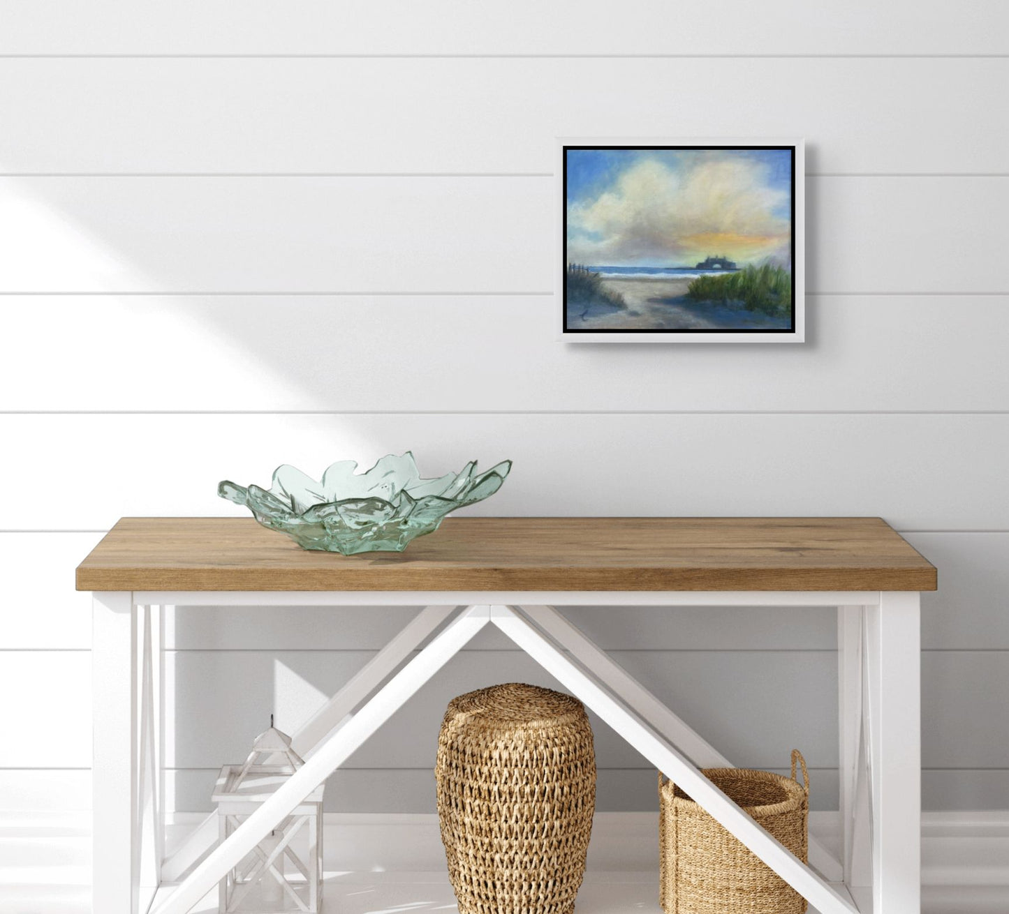 Wooden console table with a glass bowl and woven stools against a white wall with a framed Narragansett Beach & Towers painting.