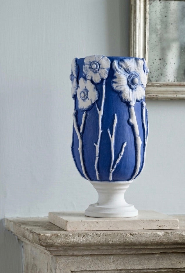 Hand-thrown porcelain vessel in deep cobalt blue, with white anemone flowers in relief around the rim, displayed on an aged limestone mantel.