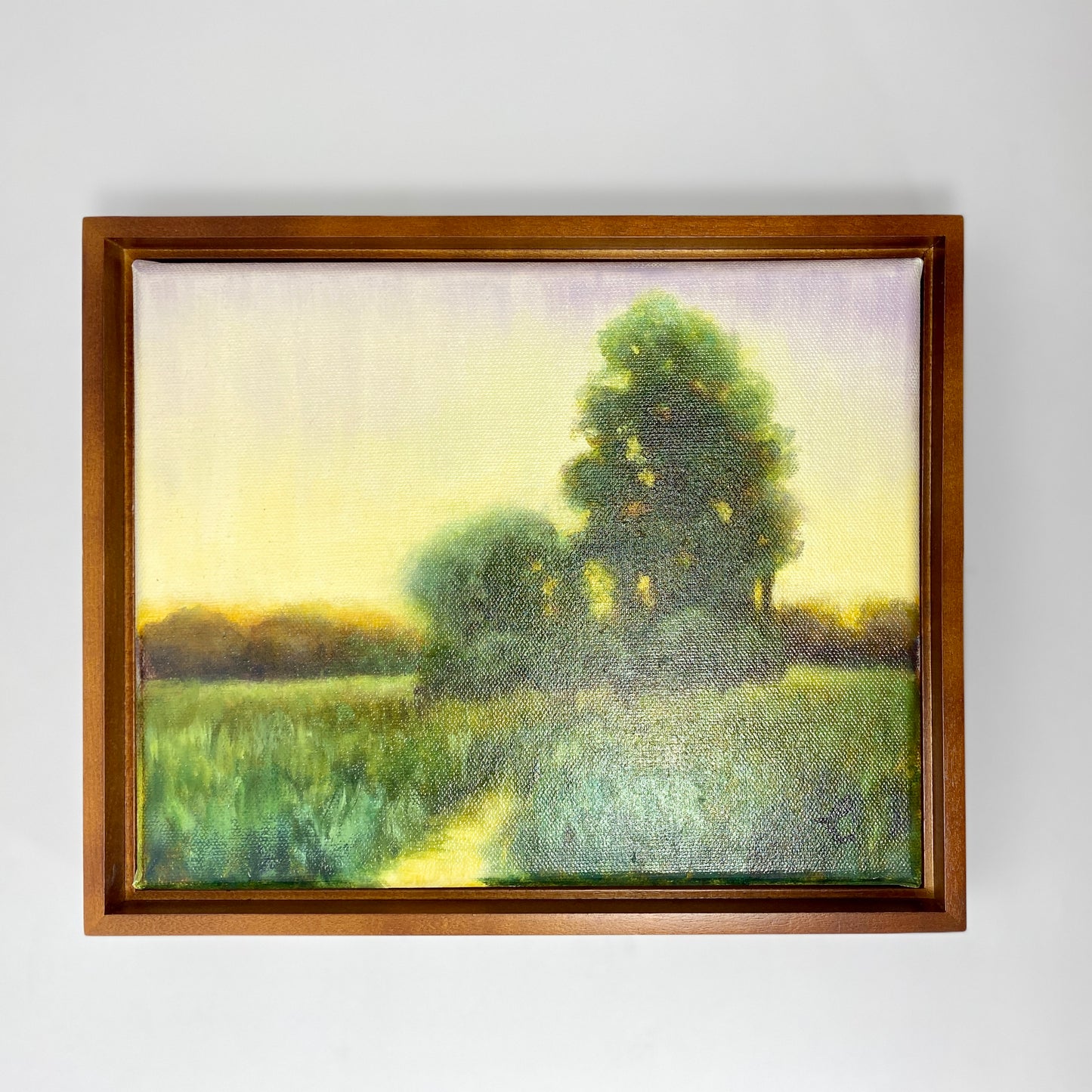 Framed original oil painting of a landscape with trees and a path on a white wall