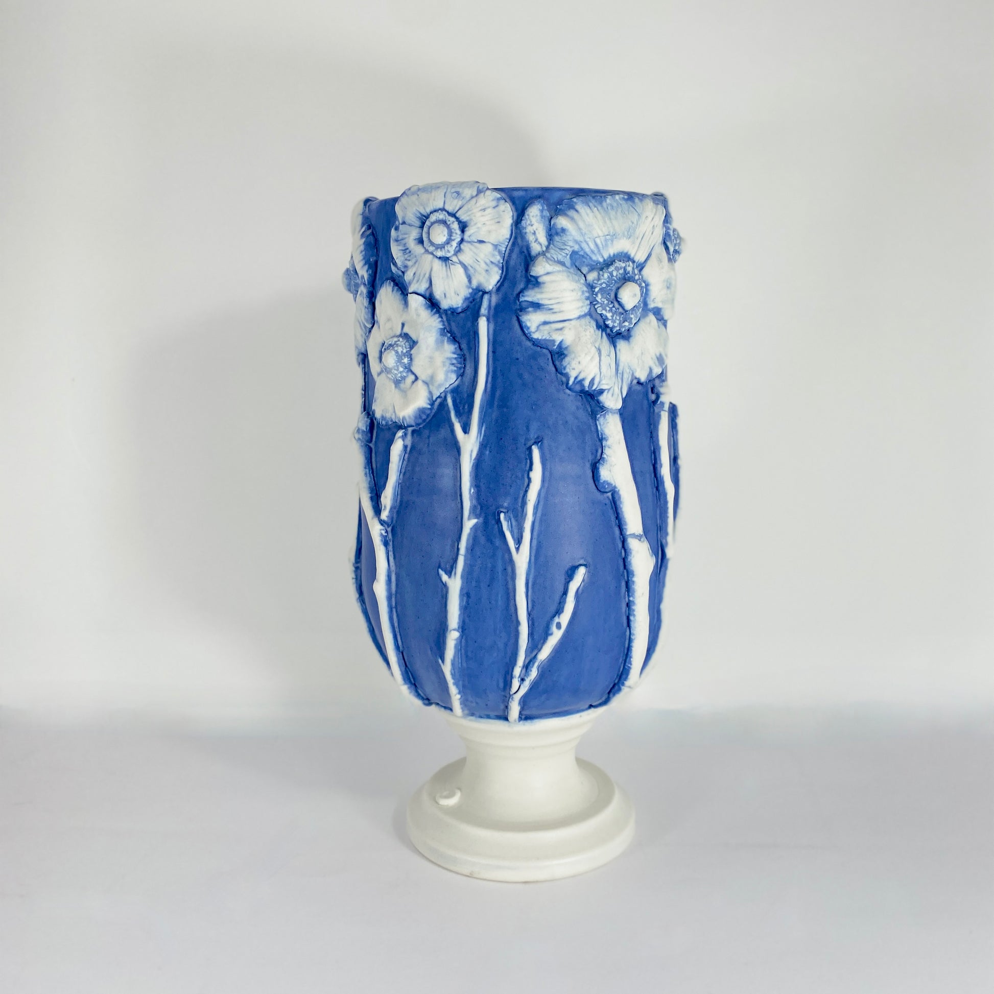Product image shot of hand-thrown porcelain vessel in deep cobalt blue, with white anemone flowers in relief around the rim