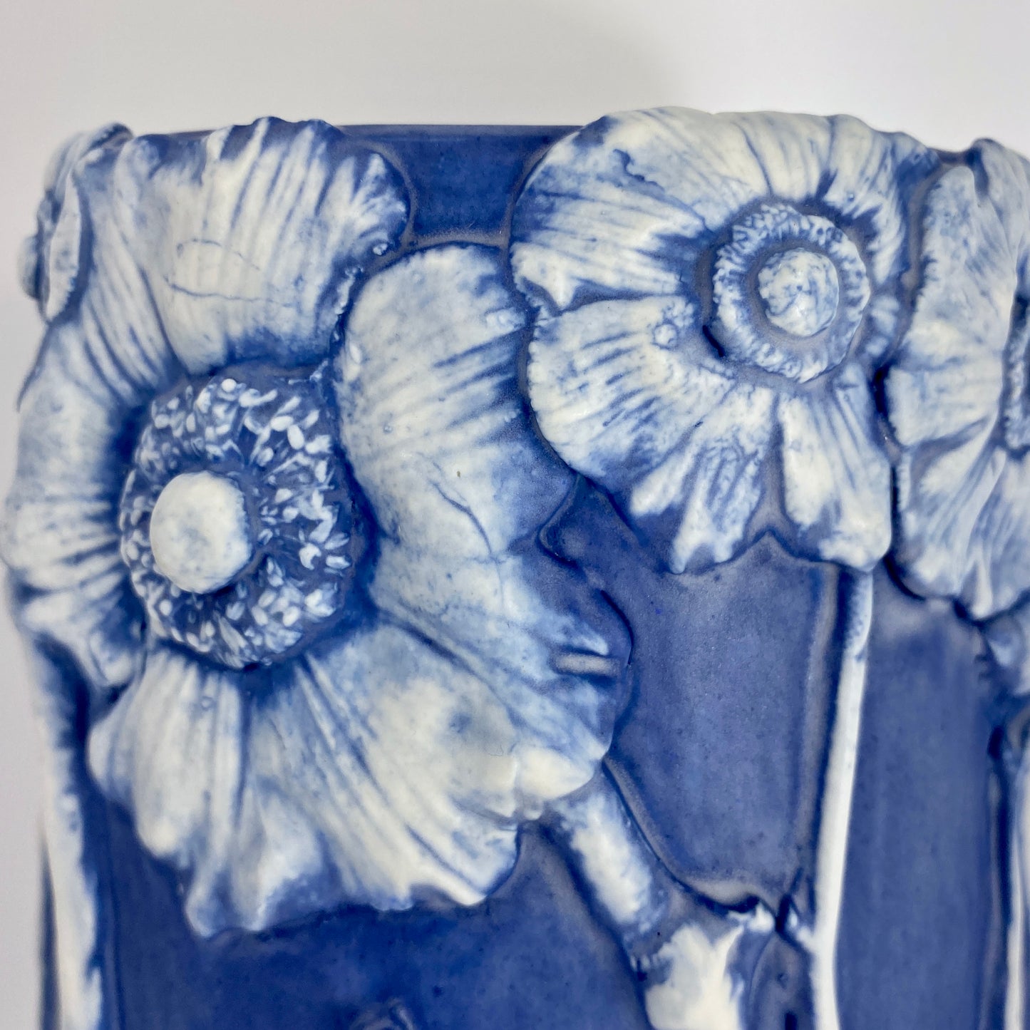 Close-up of the cobalt vessel's surface showing four white anemone blooms in porcelain relief, hand-pressed from molds taken of real garden flowers.