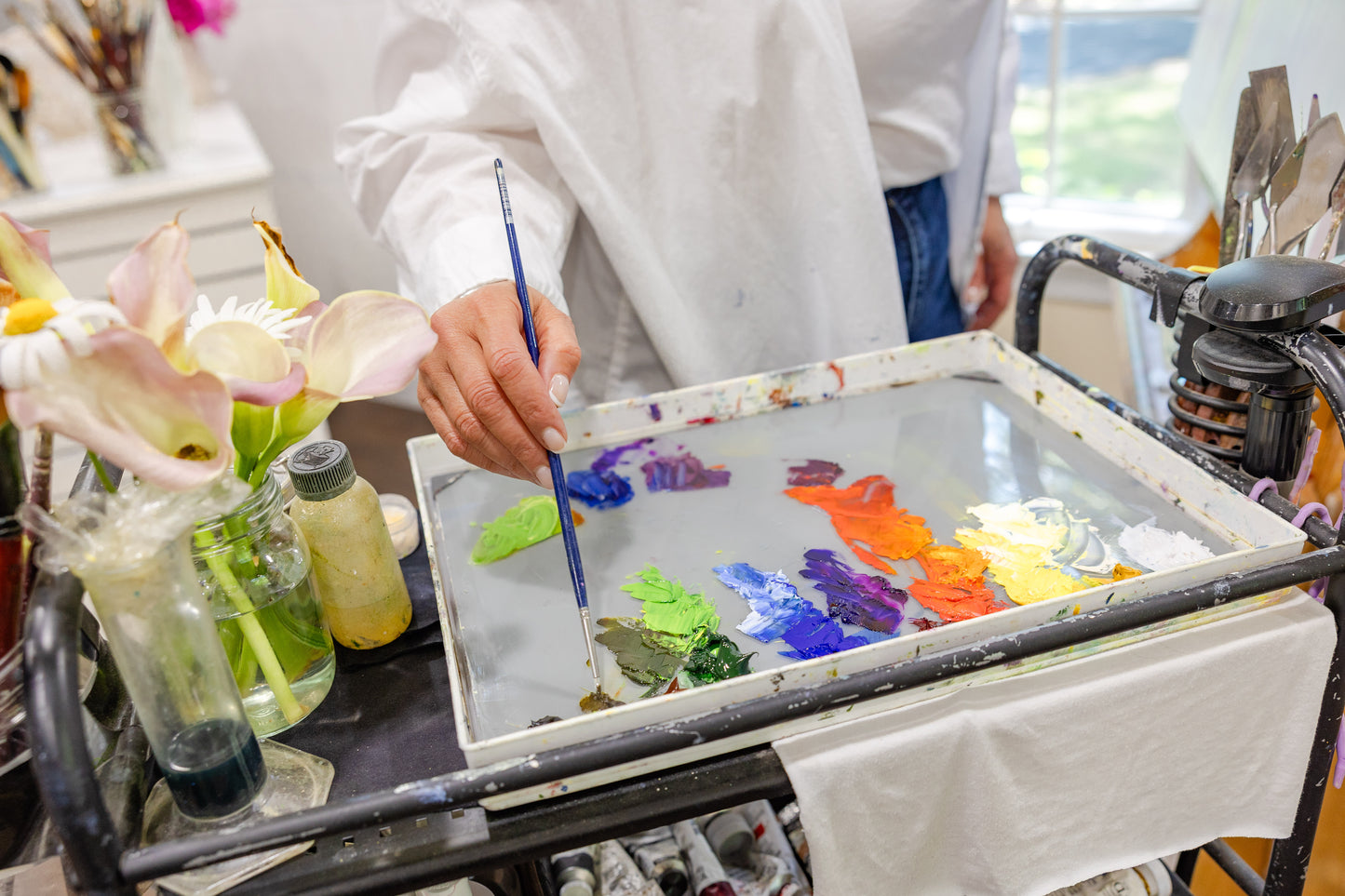 Artist Carla Thomson painting with oil paints on a palette, surrounded by art supplies.
