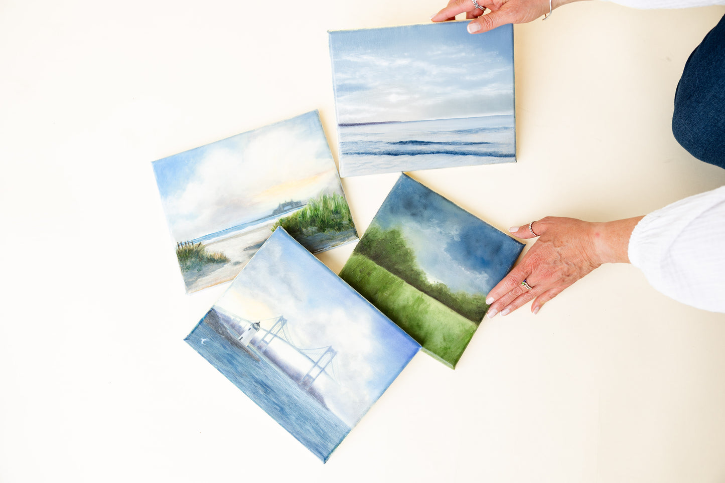 Set of oil paintings of coastal RI landscapes held by artist Carla Thomson on a white surface.