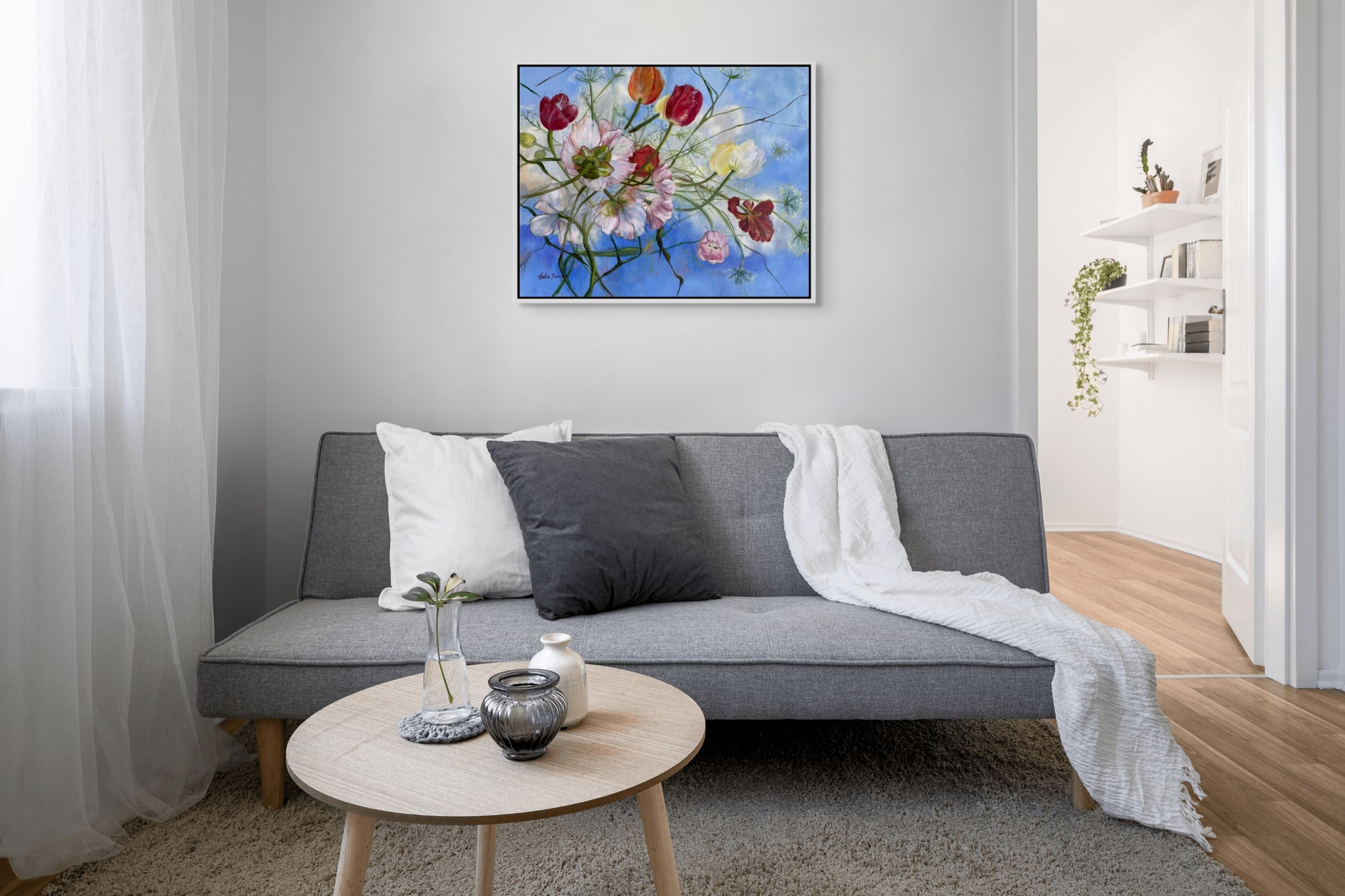 Modern living room with a gray sofa, round wooden coffee table, and Wishful Thinking a colorful original floral oil painting on the wall.