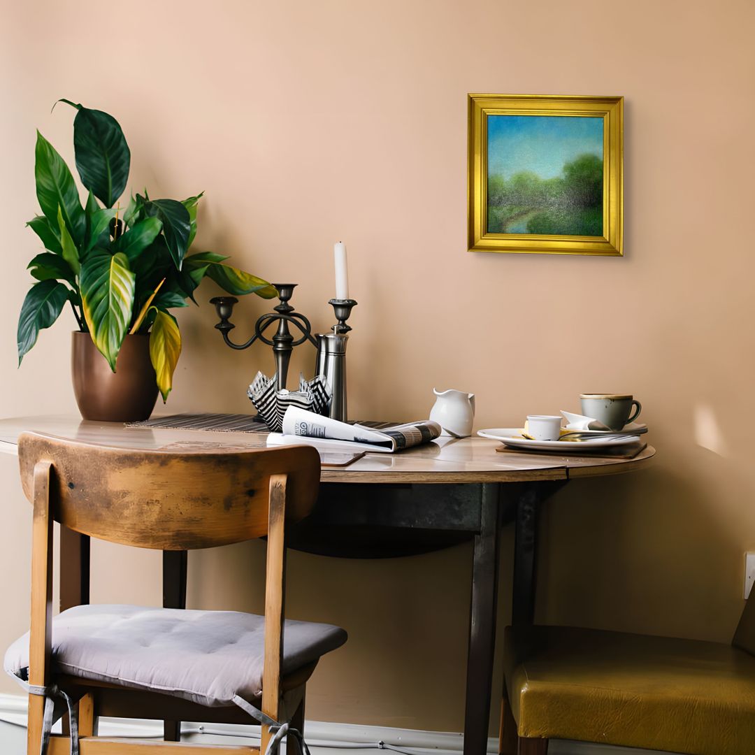 Dining room with a round table, chairs, and a gold framed original oil landscape painting on the wall.